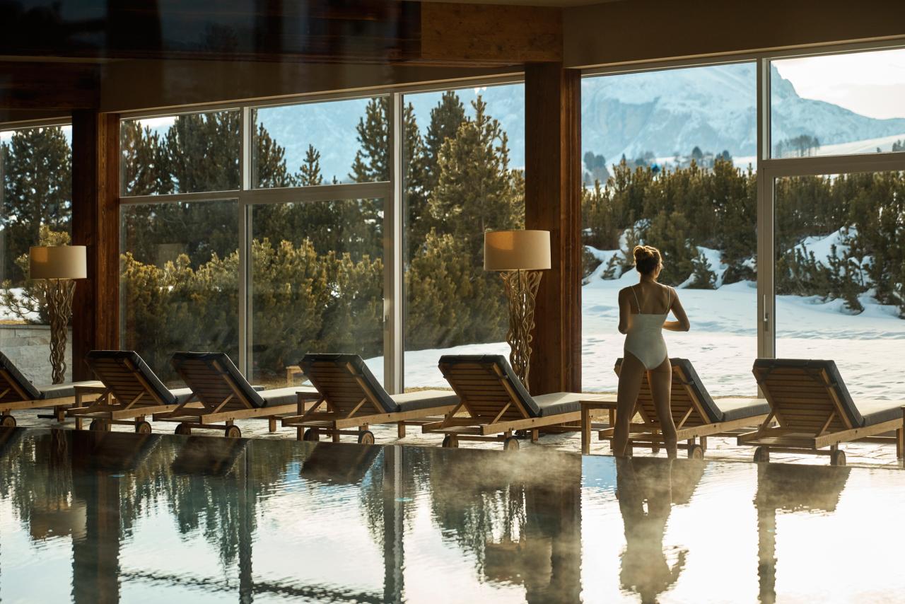Frau an einem Indoorpool mit großen Fenstern mit Blick auf verschneite Landschaft