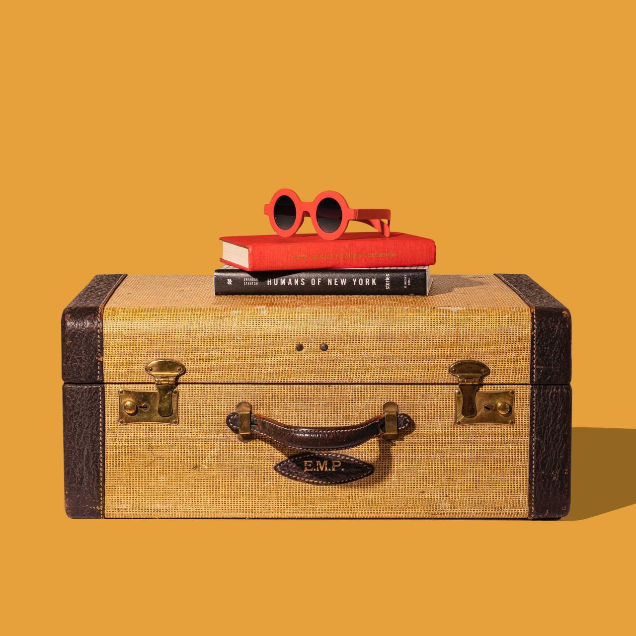 Brauner Koffer mit zwei Büchern und einer roten Sonnenbrille drauf