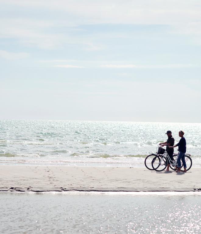 Zwei Radfahrer an einem leeren Strand mit dem Meer im Hintergrund