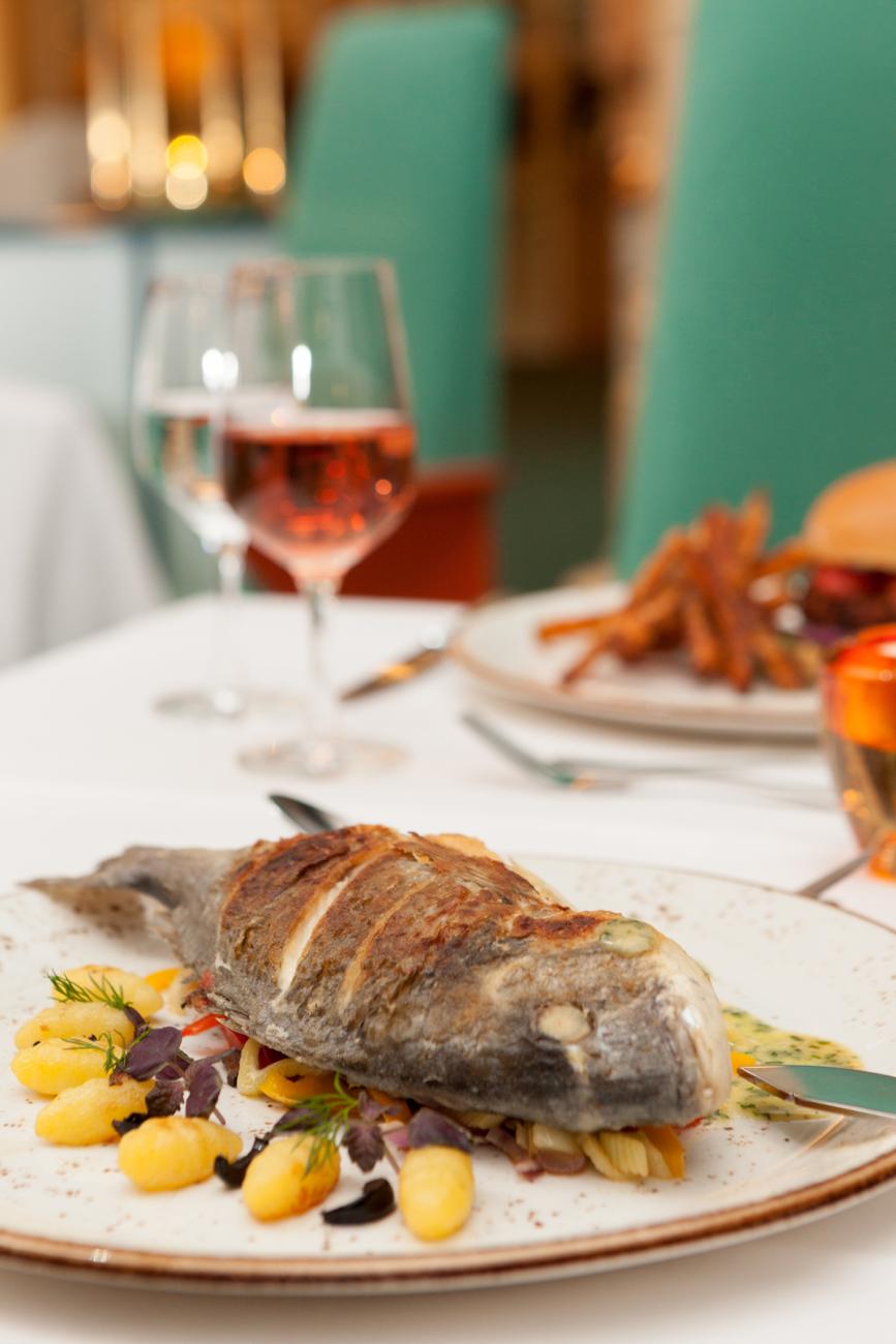 Gedeckter Tisch mit einem gefüllten Weinglas und einem Teller, auf dem ein Fischgericht liegt