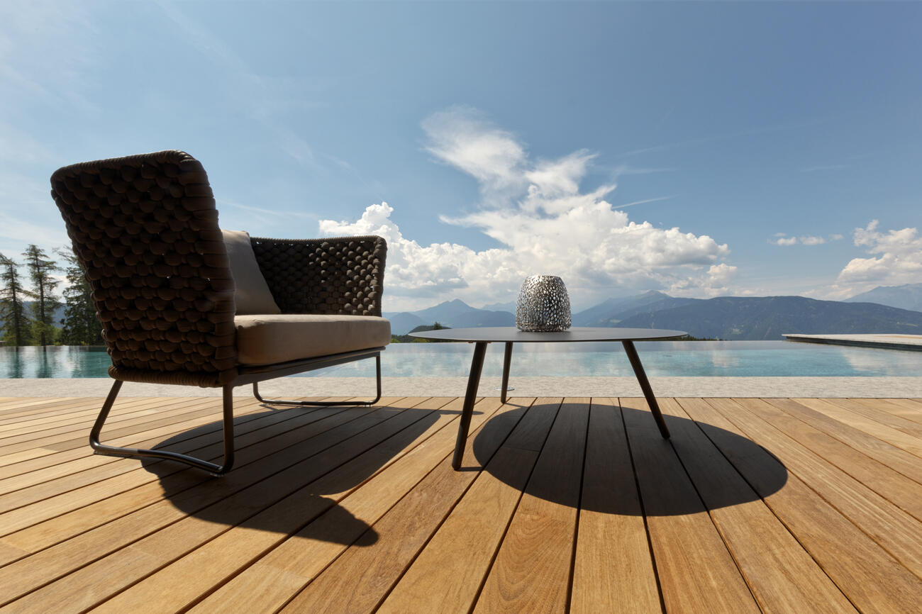 Stuhl mit rundem Tisch auf einer Holzterrasse mit Pool und Bergblick im Chalet Mirabell