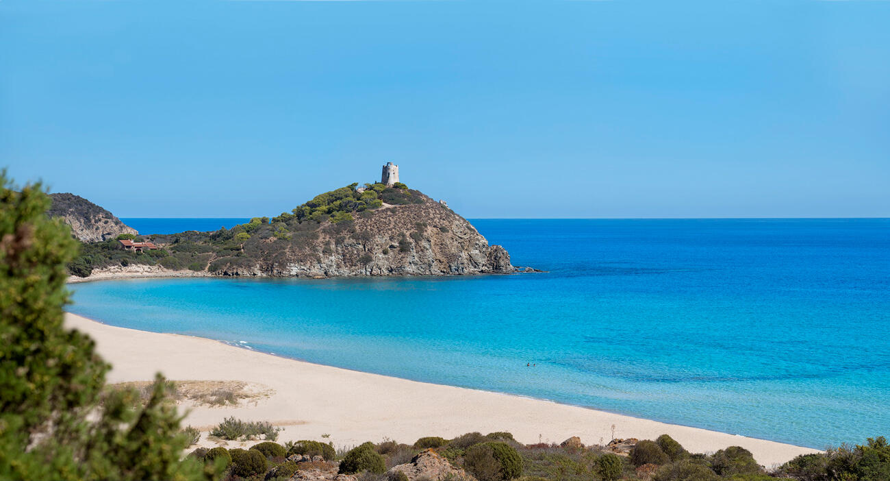 blick auf eine kleine Bucht in Sardinien. Im Hintergrund ist ein Hügel mit einem Turm und das Meer.