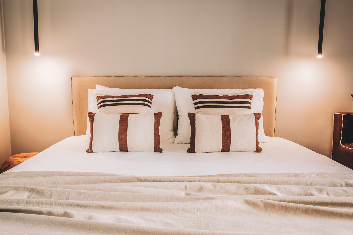 Bett mit Holzettkante und rot weißen Kissen. Neben dem Bettkopf hängen zwei Lampen.
