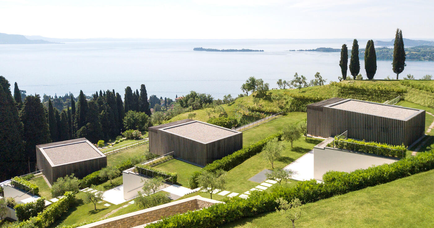Kleine quadratische Villas die auf einem grünen Hügel liegen und Ausblick auf einen See haben