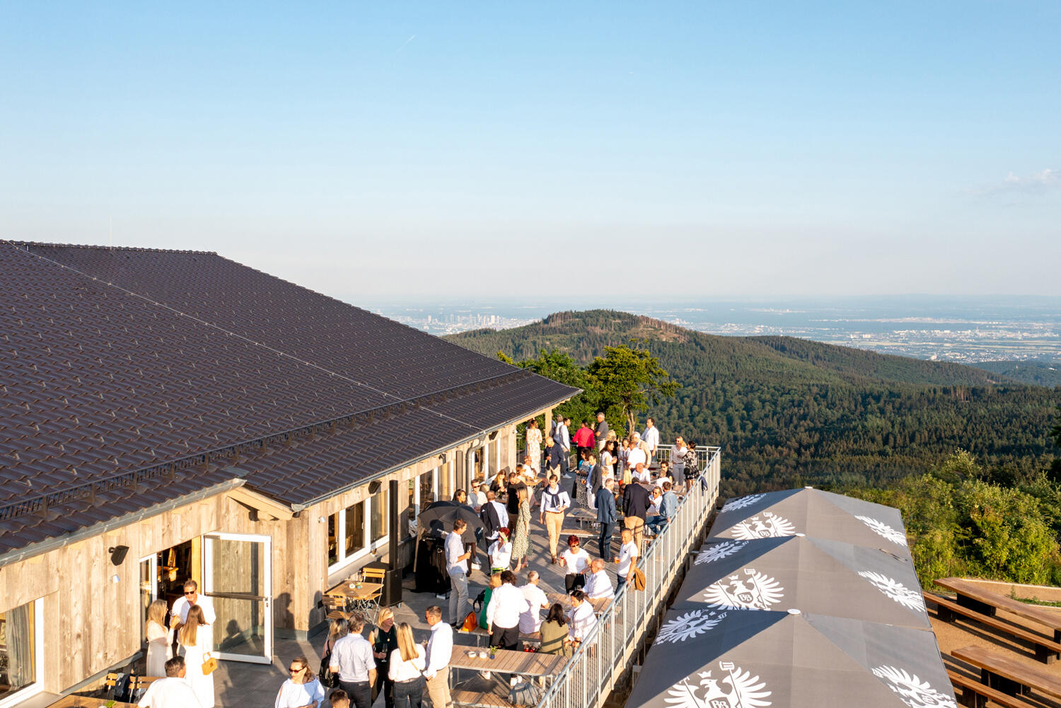 Restaurant mit großer Terrasse voller Leute auf einem Gipfel. Im Hintergrund blickt man aufs Tal