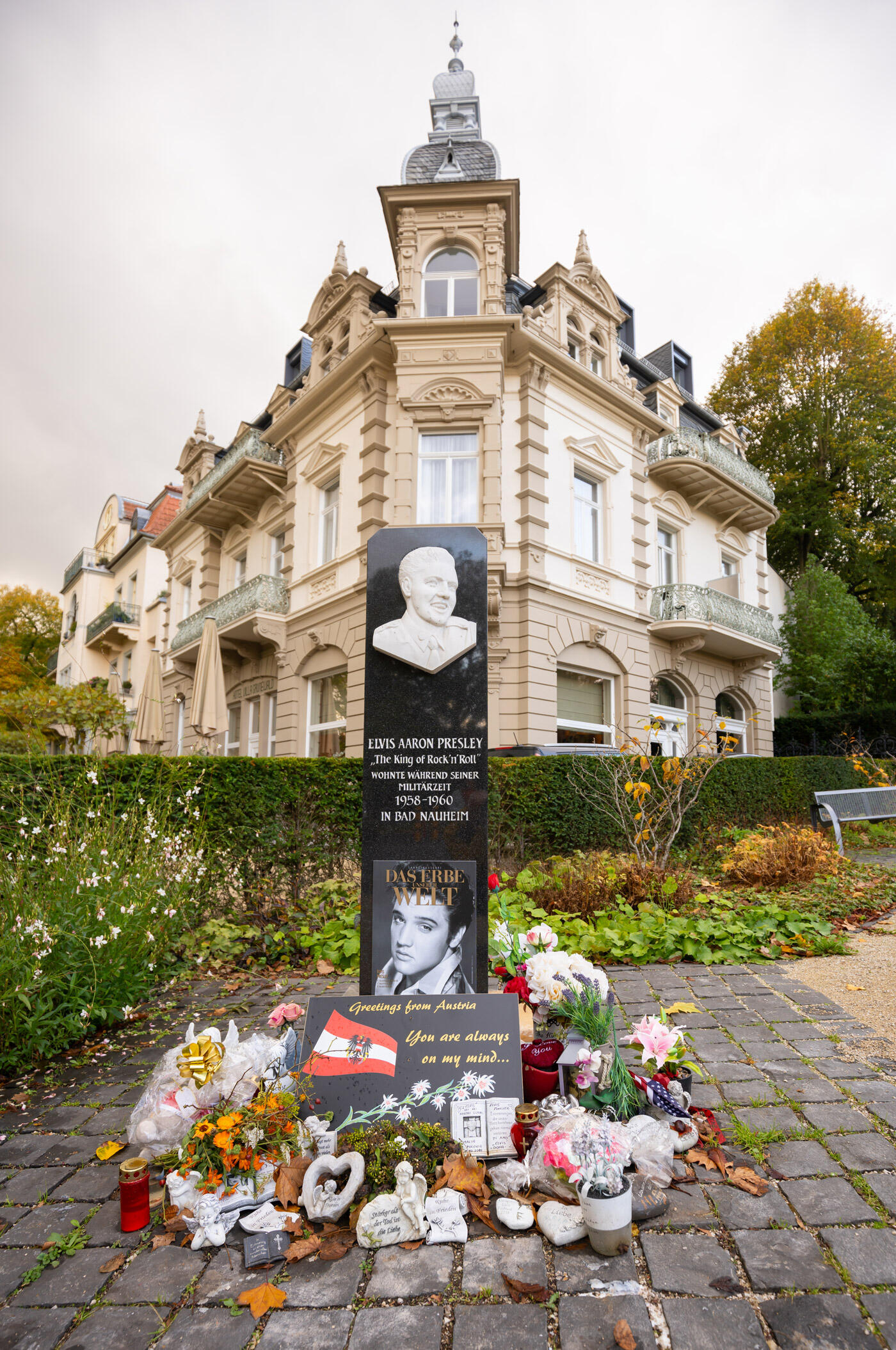 Elvis Gedenkstätte in Bad Neuheim: Eine Säulle mit Blumen und Kerzen. Im Hintergrund steht ein historisches Haus.