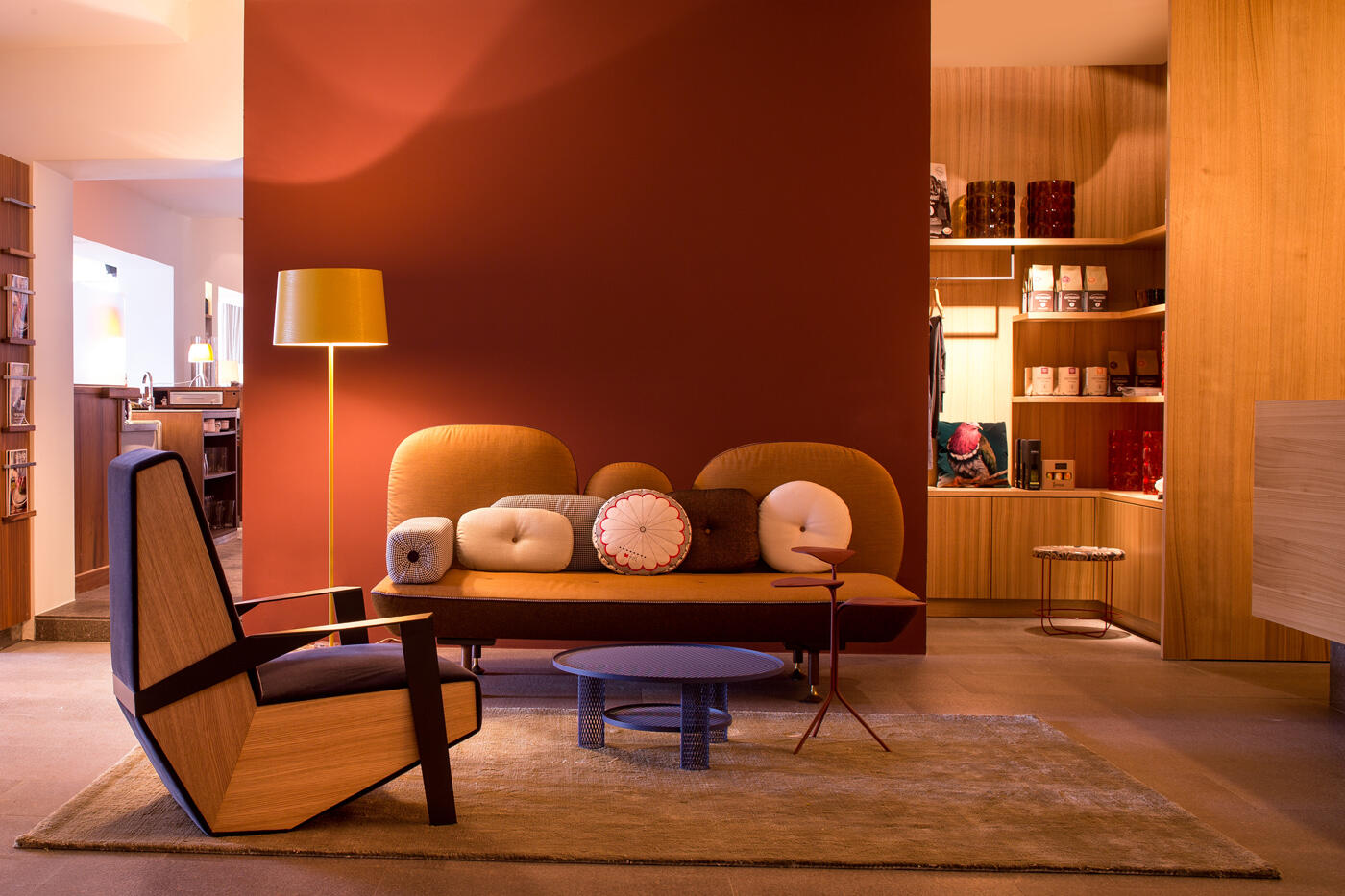 Moderner Sitzbereich in der Rezeption des Hotel Mucheles mit orangenem Sofa und hHolzsessel vor roter Wand