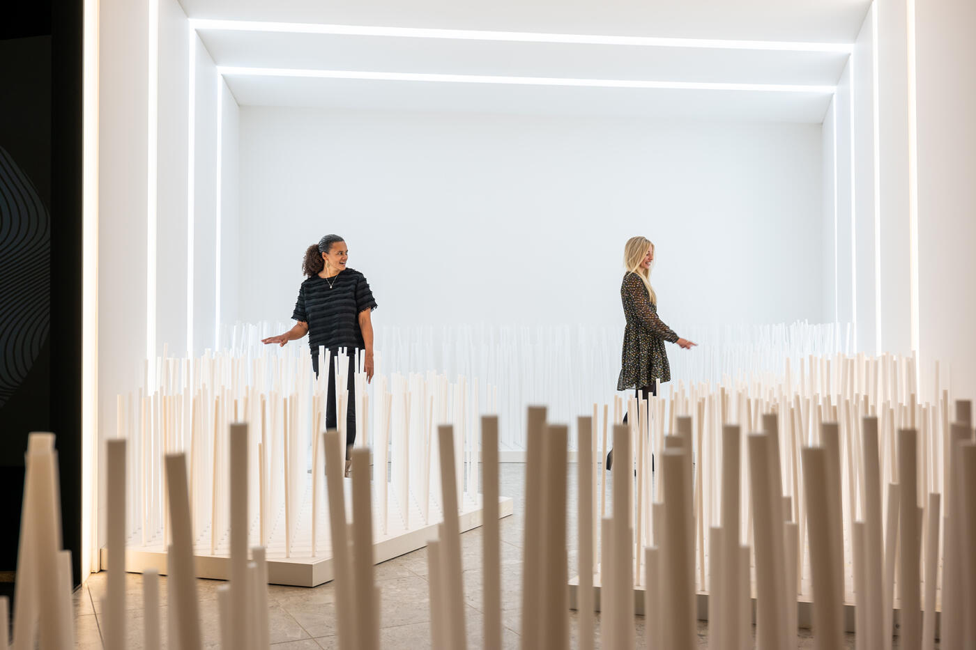 Zwei Frauen in einem Ausstellungesraum. Am Boden stehen verschiedene Holsstecken.