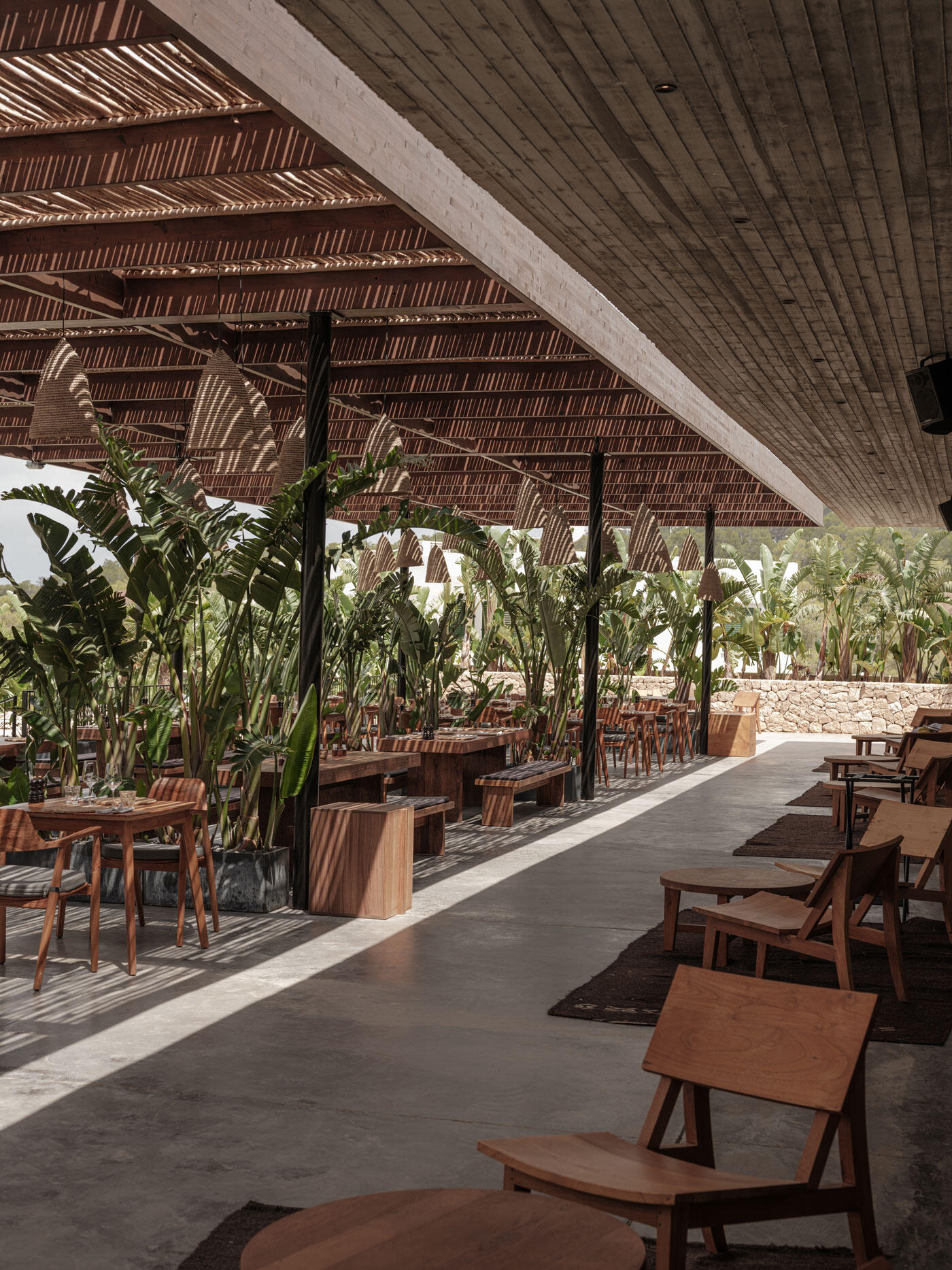 Überdachtes Outdoor-Restaurant mit vielen Tischen und Stühlen und grünen Pflanzen.