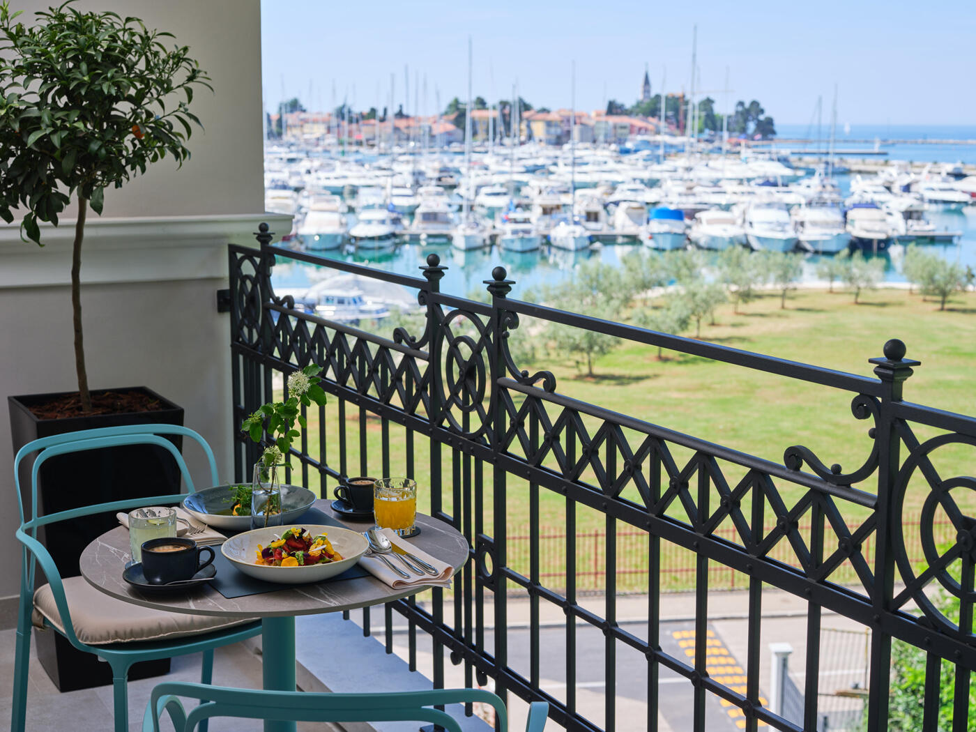 Kleine Terrasse mit einem runden Tisch, auf dem Frühstück steht. Im Hintergrund sieht man einen Hafen am Meer.