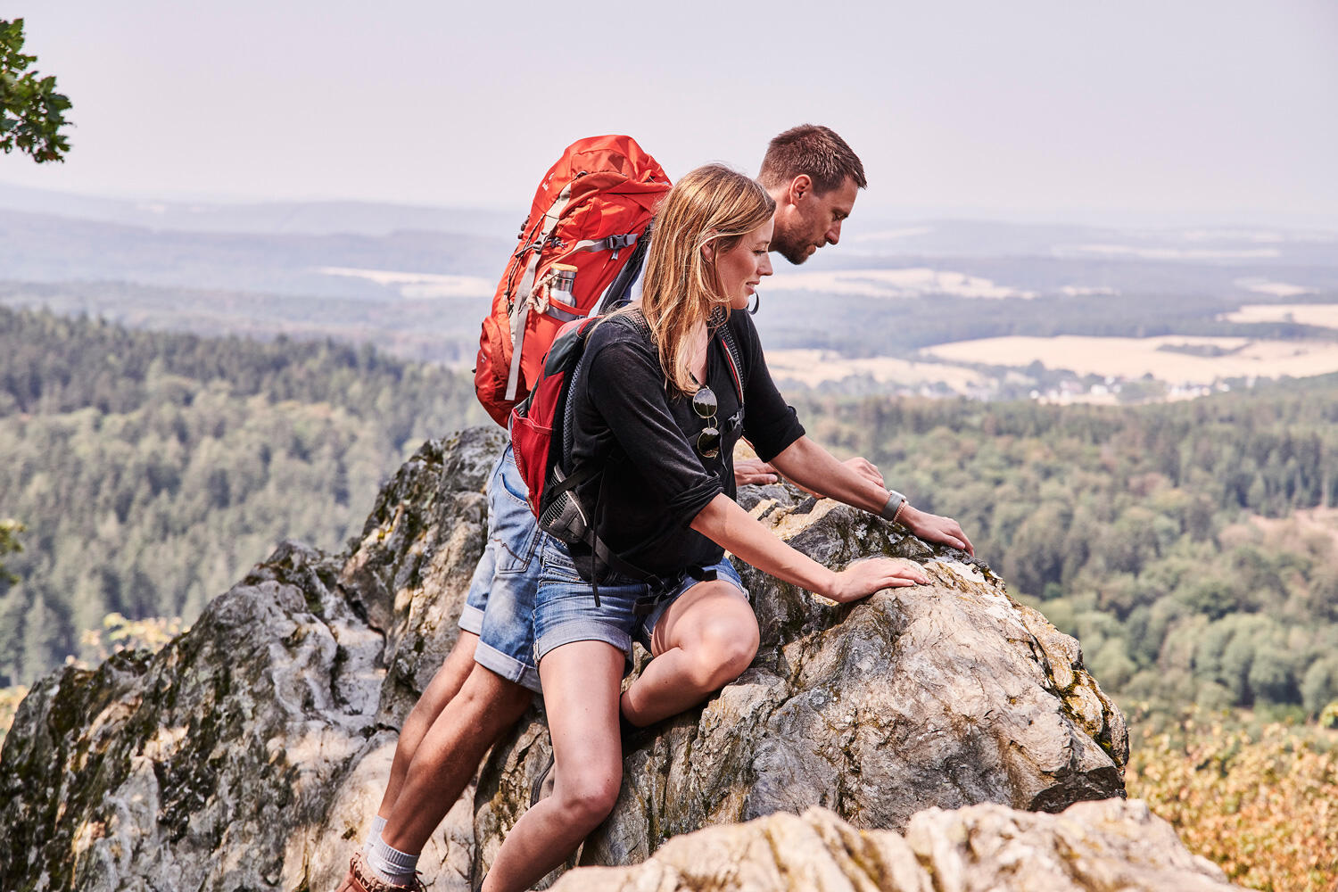 Zwei Wanderer, die auf einer Felsspitze sitzen und die Aussicht auf Wälder genießen im Taunus
